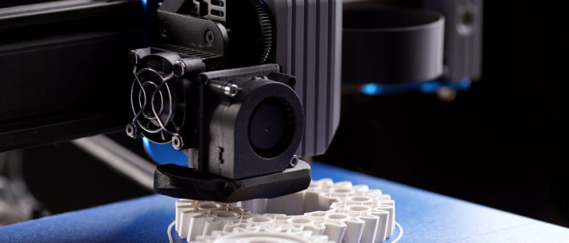 gantry with x-carriage and print head of a FDM-3D-printer that produces white helical gears on blue print bed. dark surrounding. selective focus. additive manufacturing concept